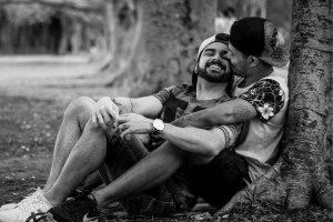 gay couple leaning against a tree kissing