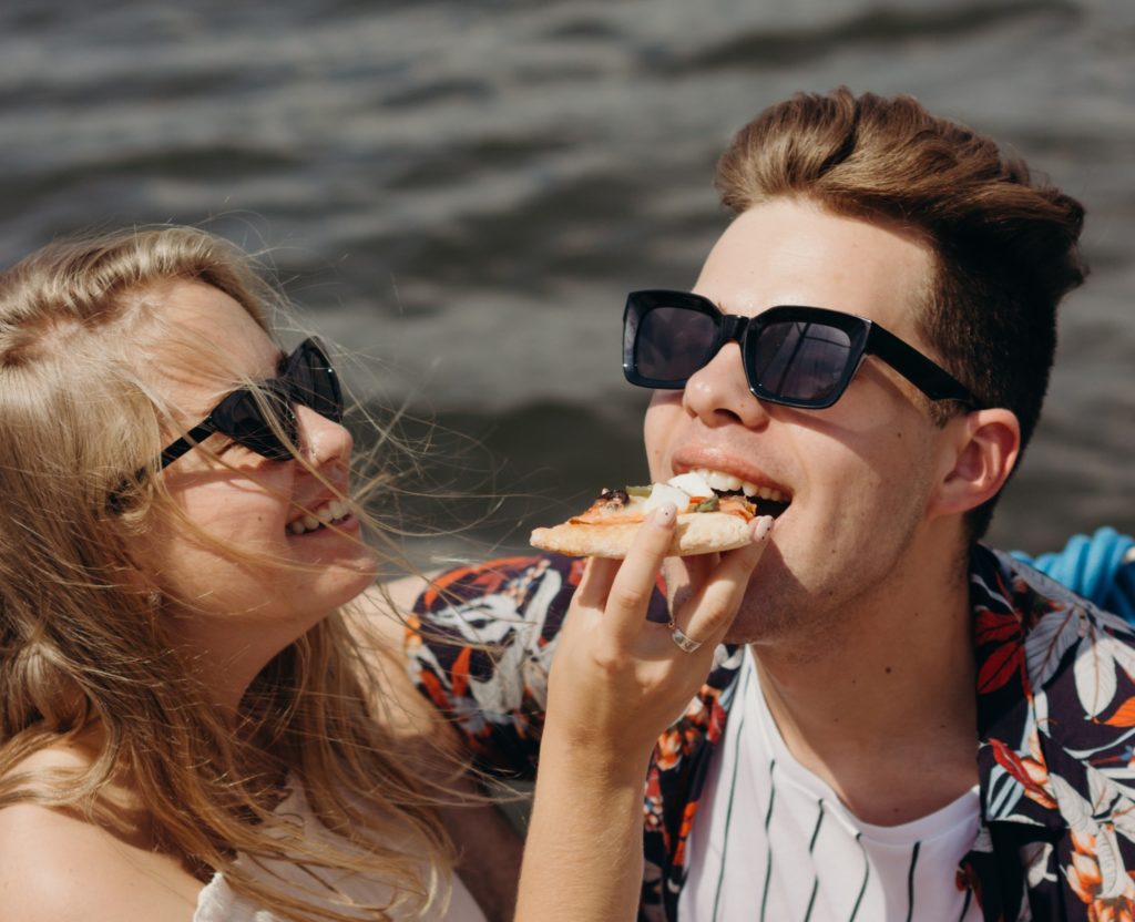 a happy young couple. one person is feeding the other a slice of pizza, and they are both smiling.