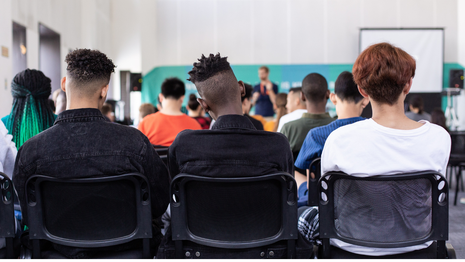 School assembly, can see the back of three boys facing the front of the hall