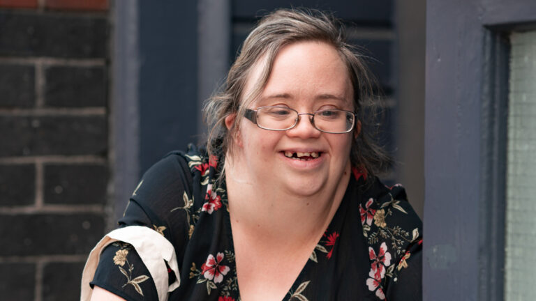 Ellen Goodey smiling, with her hands clasped on her knee.