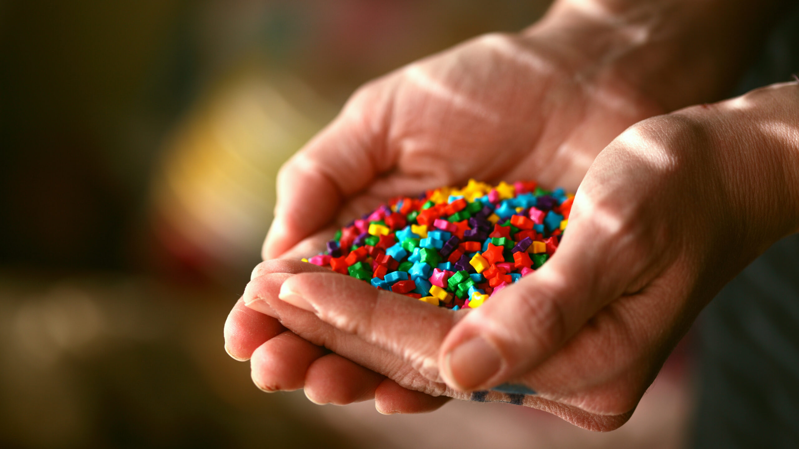 a person's hands cupped, full of tiny colourful stars