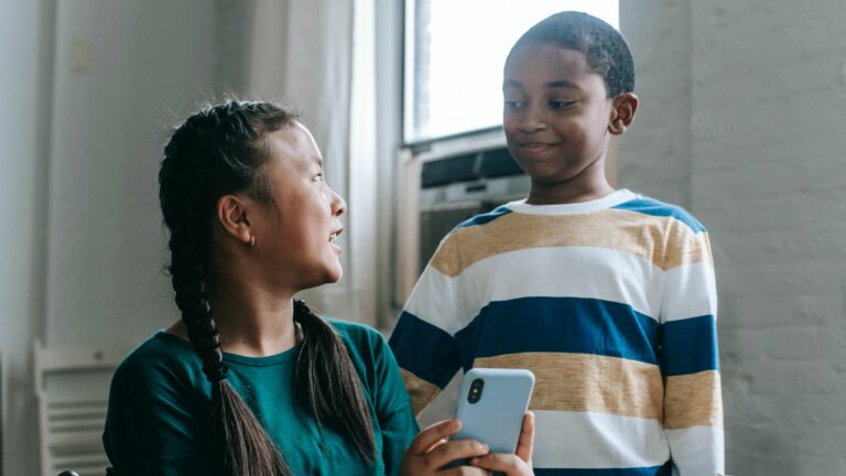 two young people looking at each other and smiling. One is holding a phone.