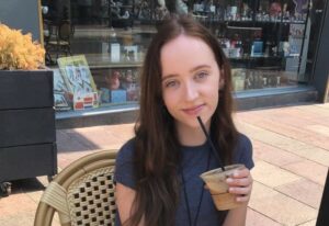 Annie sitting outside a cafe with a coffee smiling