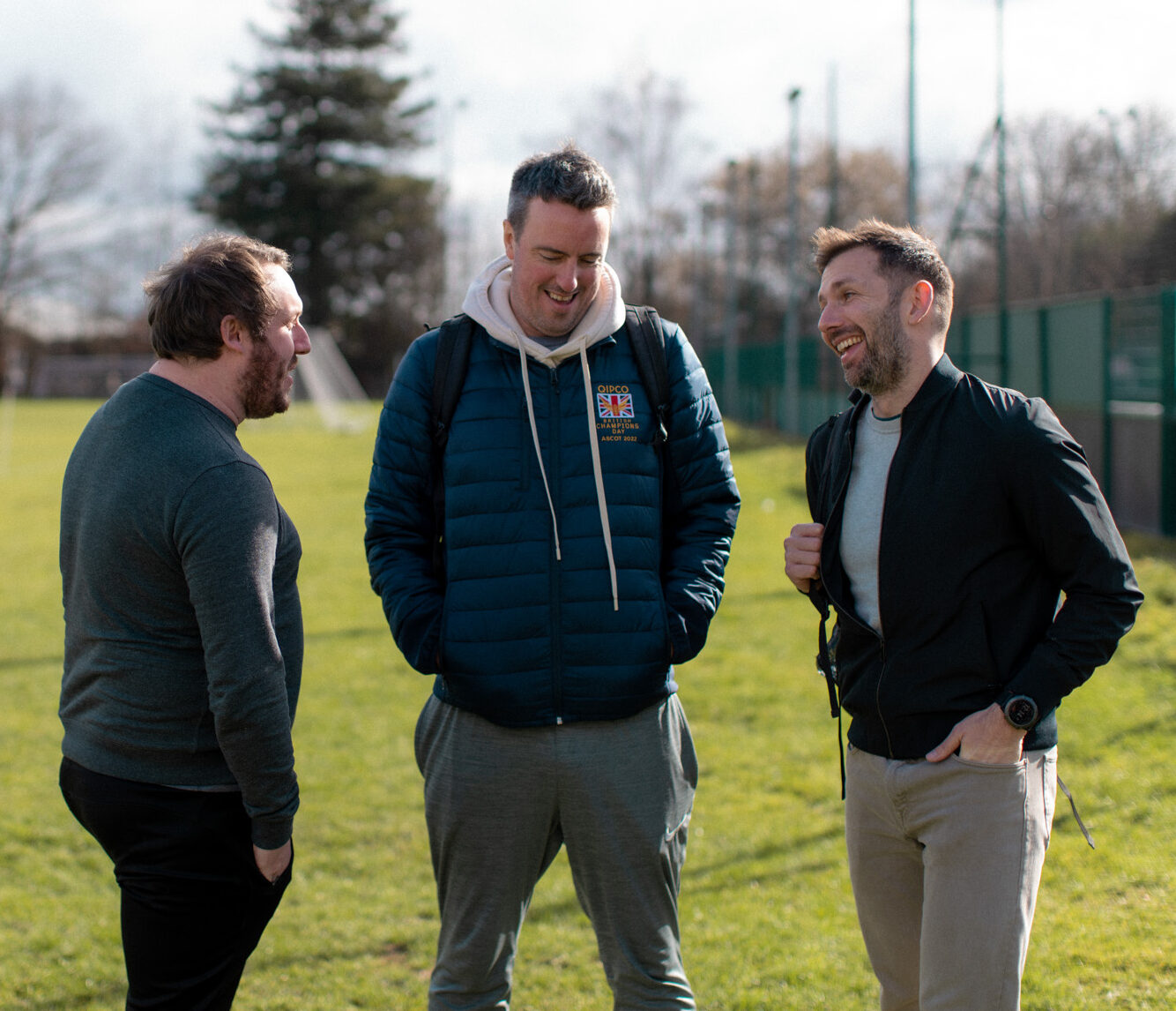 Three men stood chatting at a football pitch