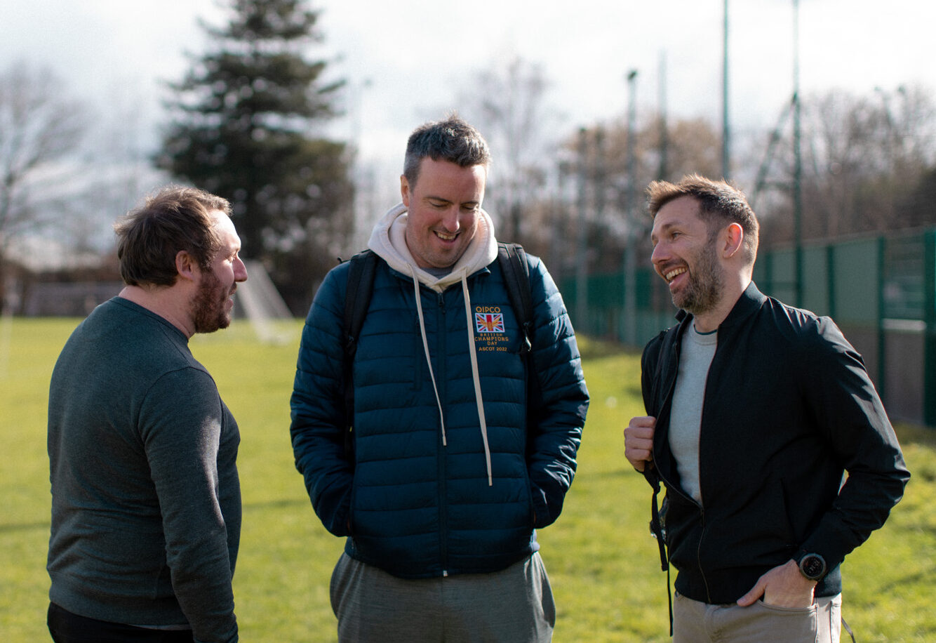 Three men stood chatting on a football field
