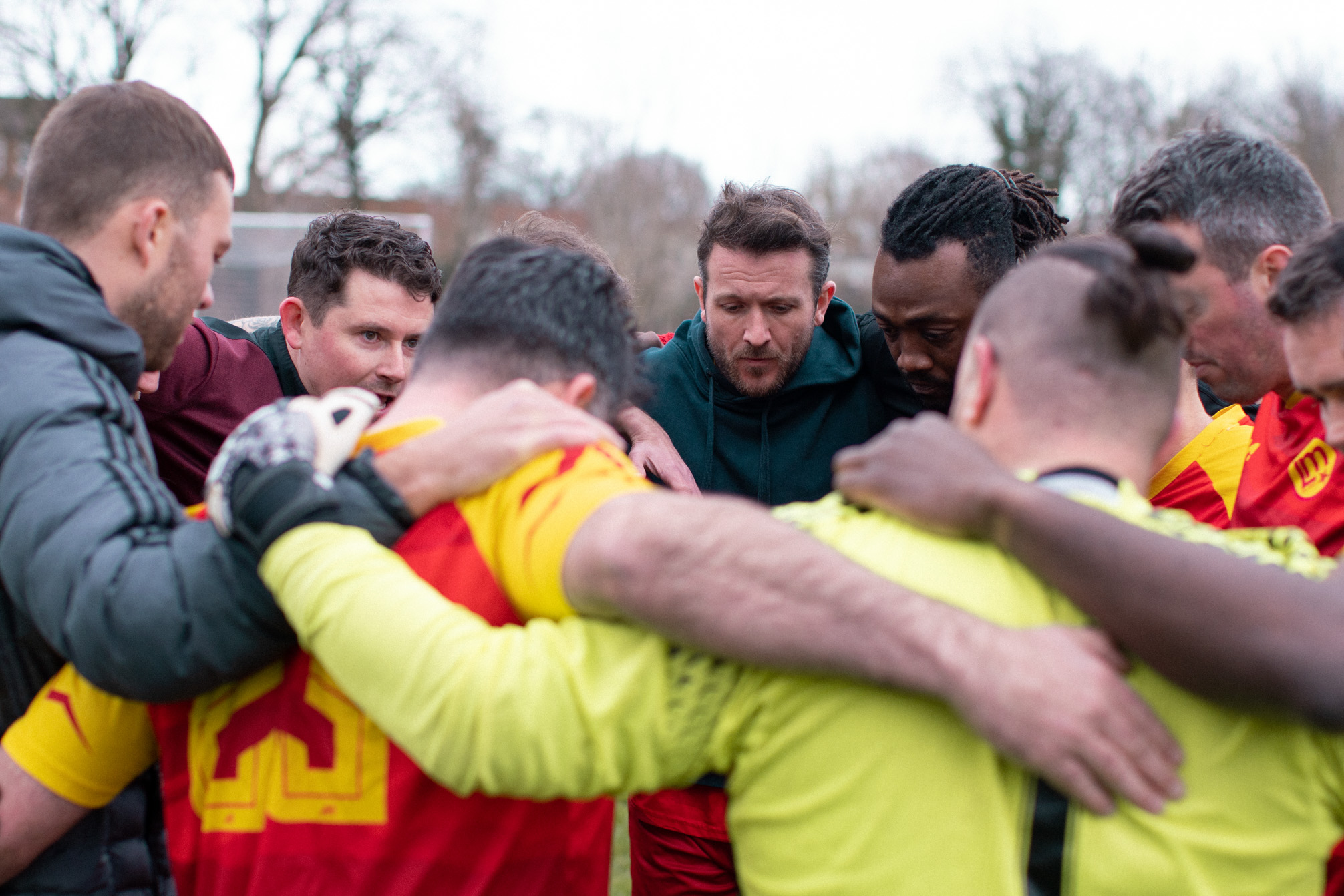 Close up view of a group of men in football kits standing in a huddle, arm in arm