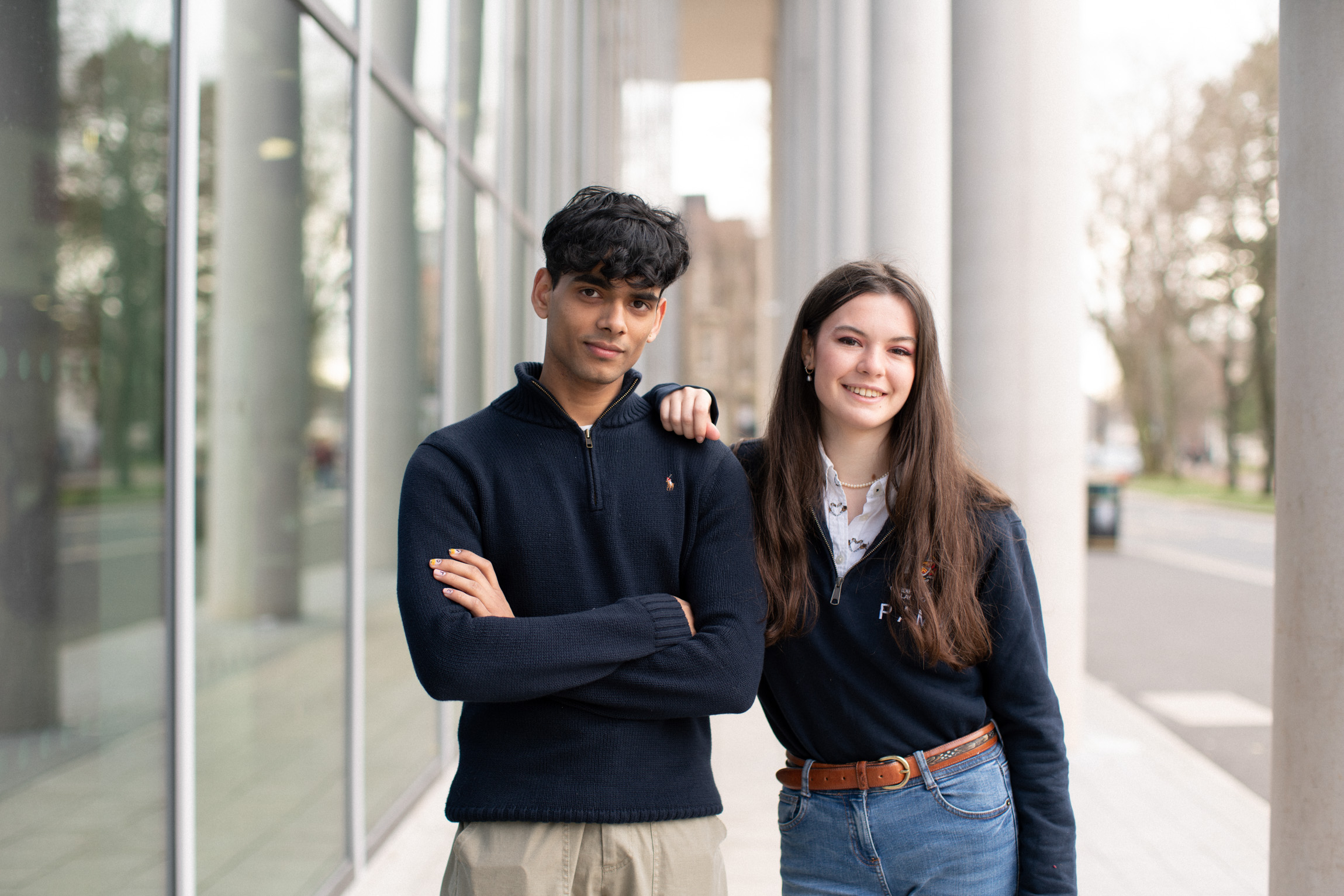 A young woman and man stood outside a building looking at the camera