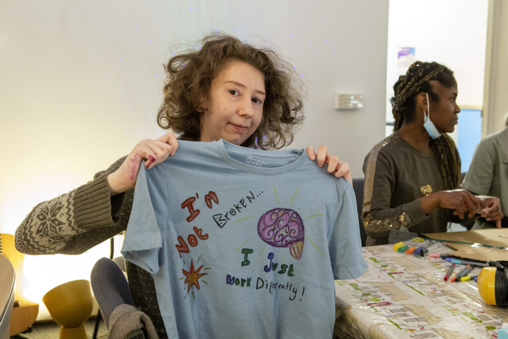 Someone holding up a decorated t-shirt that says "I'm not broken...I just work differently!"