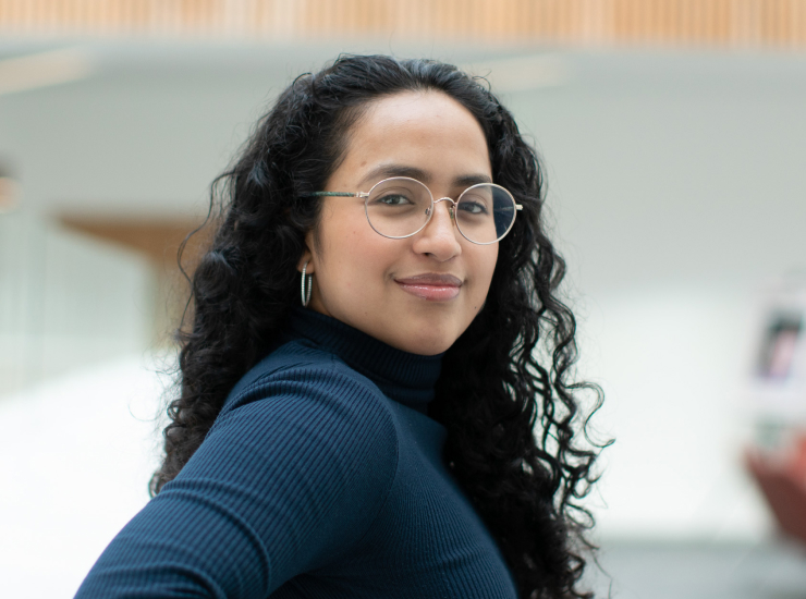 Young woman with circular glasses and curly black hair smiling confidently