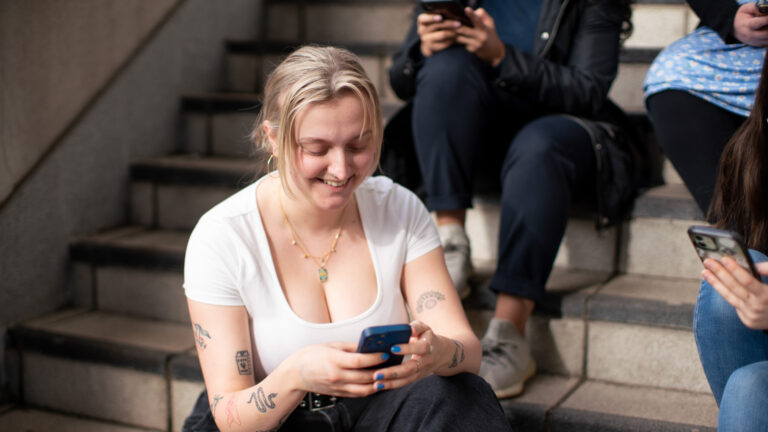 Woman looking at her phone smiling, her friends around her also on their phones