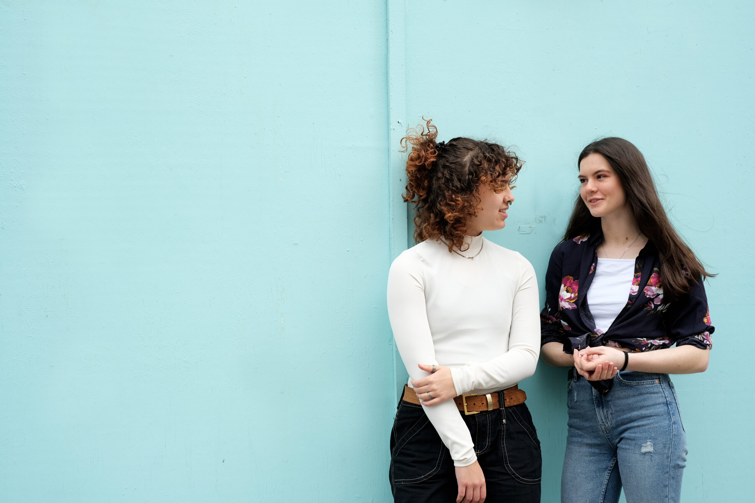 Two young women sat chatting outside against a blue wall