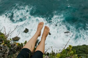 Bare feet dangling over a cliff with the sea below them