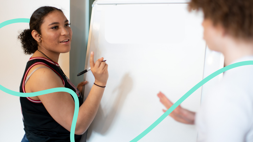 Two students stood in front of a whiteboard discussing what to write