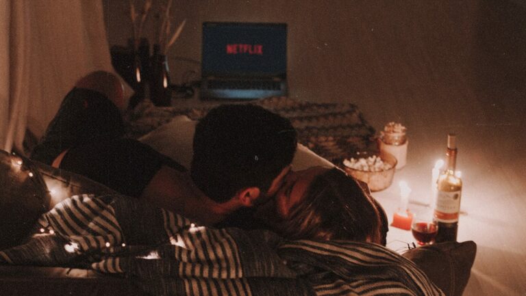 a couple cuddled in bed with candles and snacks watching netflix