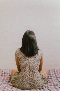 The back of a woman's head who's sitting on the bed facing the wall.