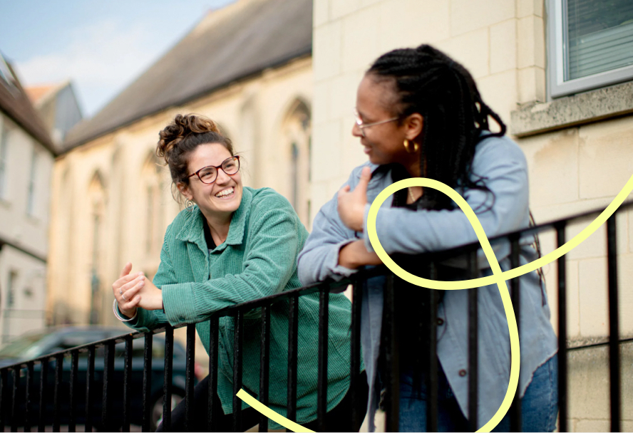 Two women leaning on a railing, smiling and chatting.