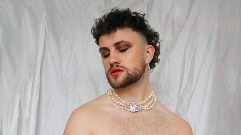 Photo of Max wearing a pearl necklace and no clothes and with eyeshadow on.