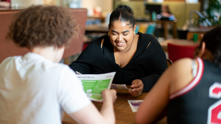 Three young people sat at a desk looking at handouts