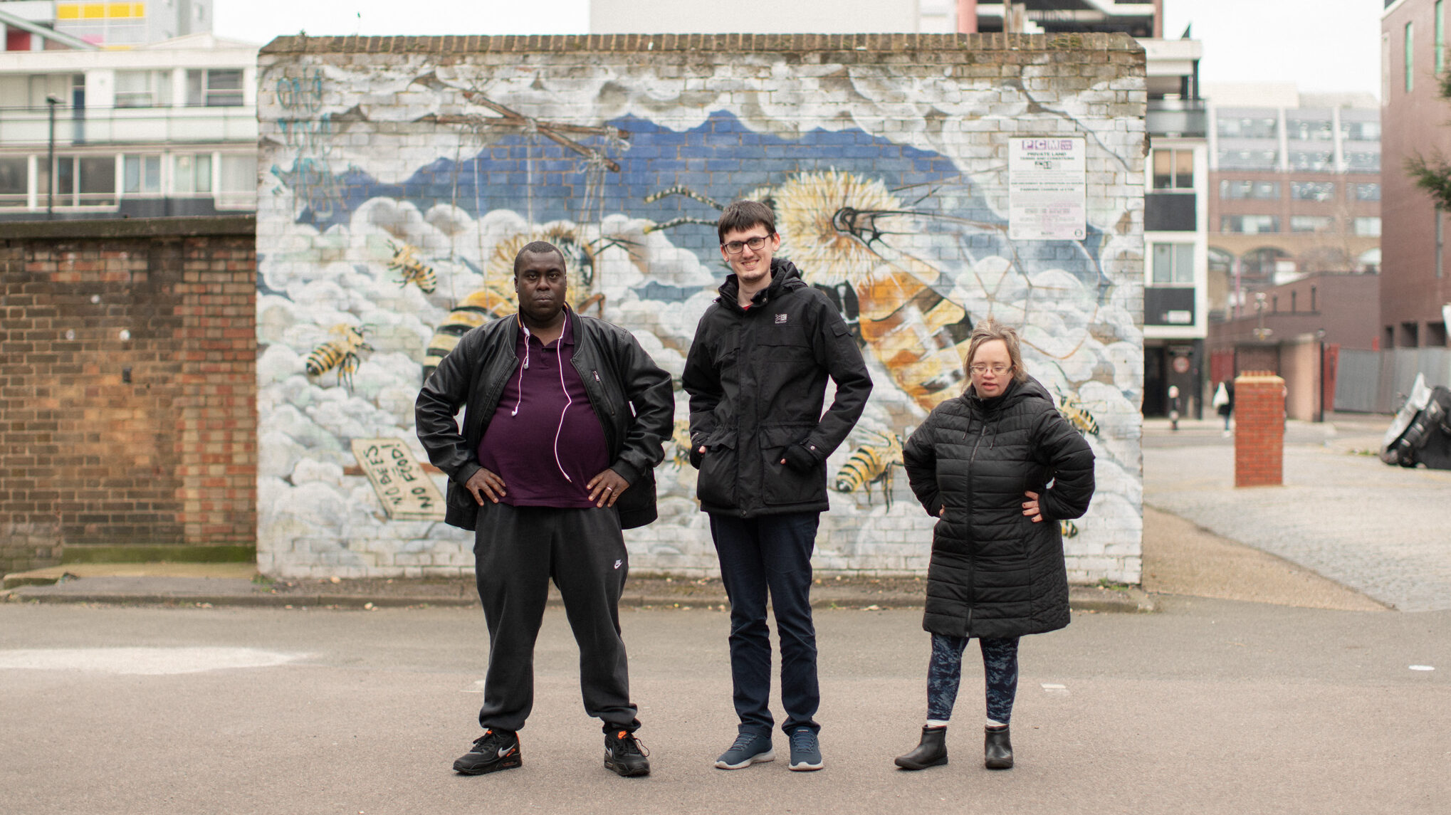 Three people stood in front of a brick wall with a mural