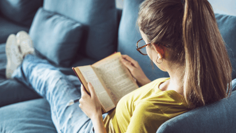 A girl reading a book lying on the sofa