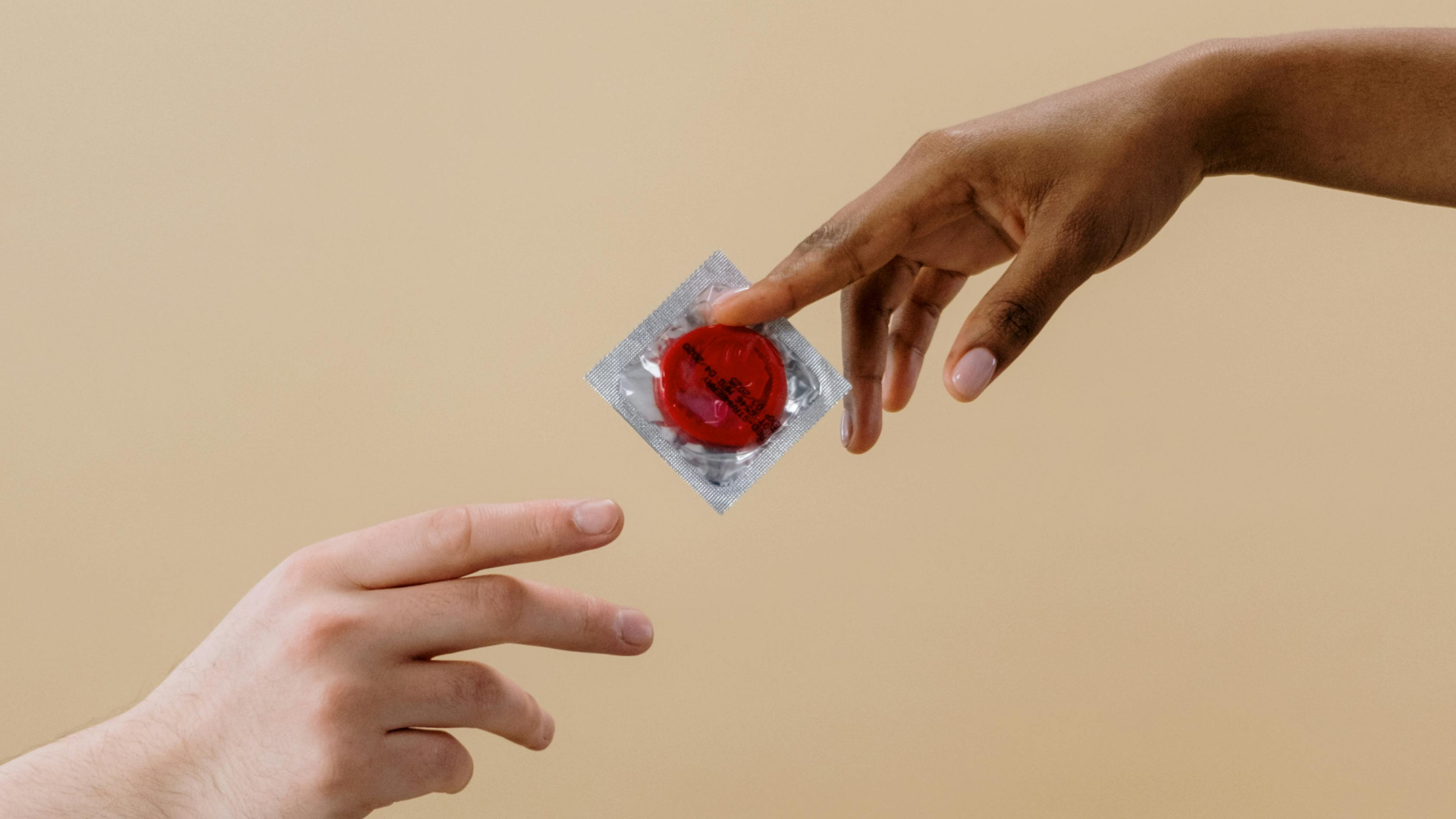 One hand holding a condom passing it to the hand of another person.