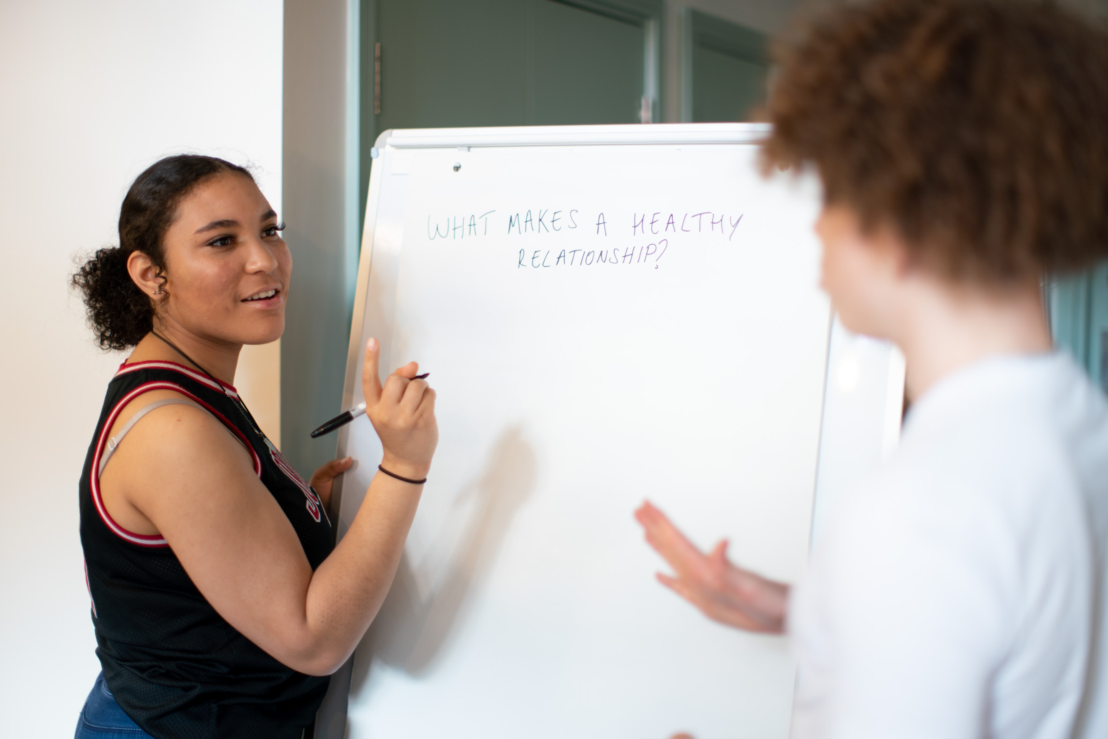 two students discuss next to a whiteboard that says "What makes a healthy relationship?"