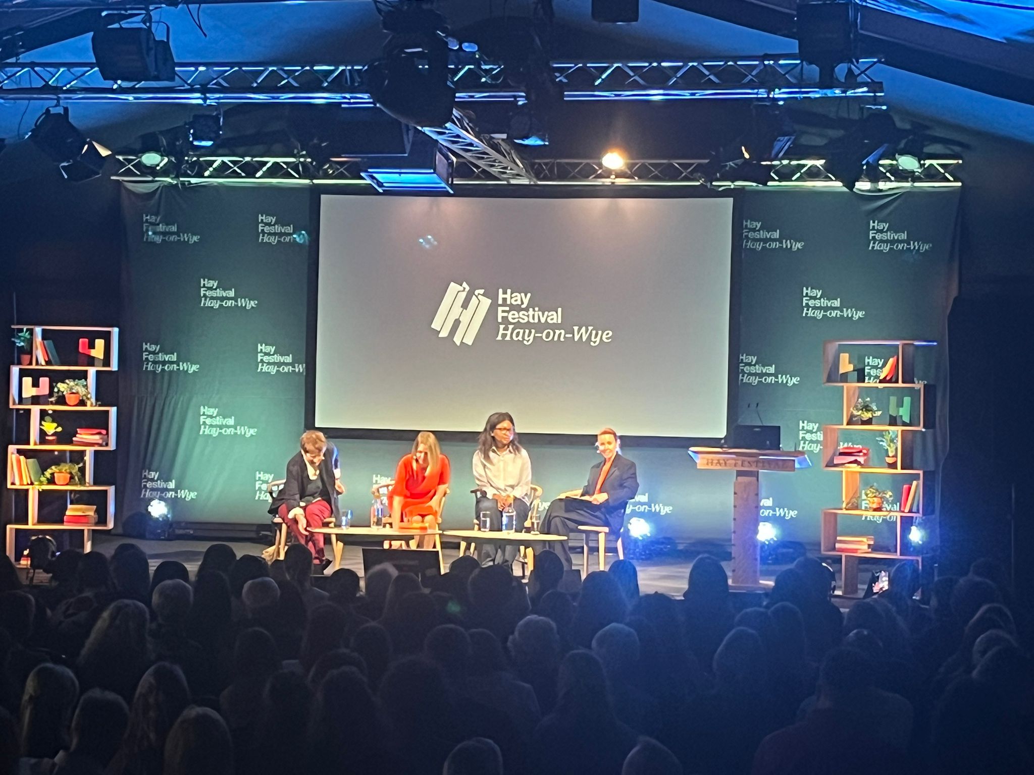 4 panelists on stage with a logo on a screen behind that reads "Hay Festival: Hay-on-Wye"