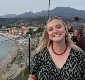 The author Sian stands on a patio overlooking a beach. She is smiling at the camera