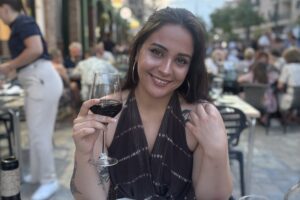 The author Rachel sits outside holding a wine glass and wears a halter neck top