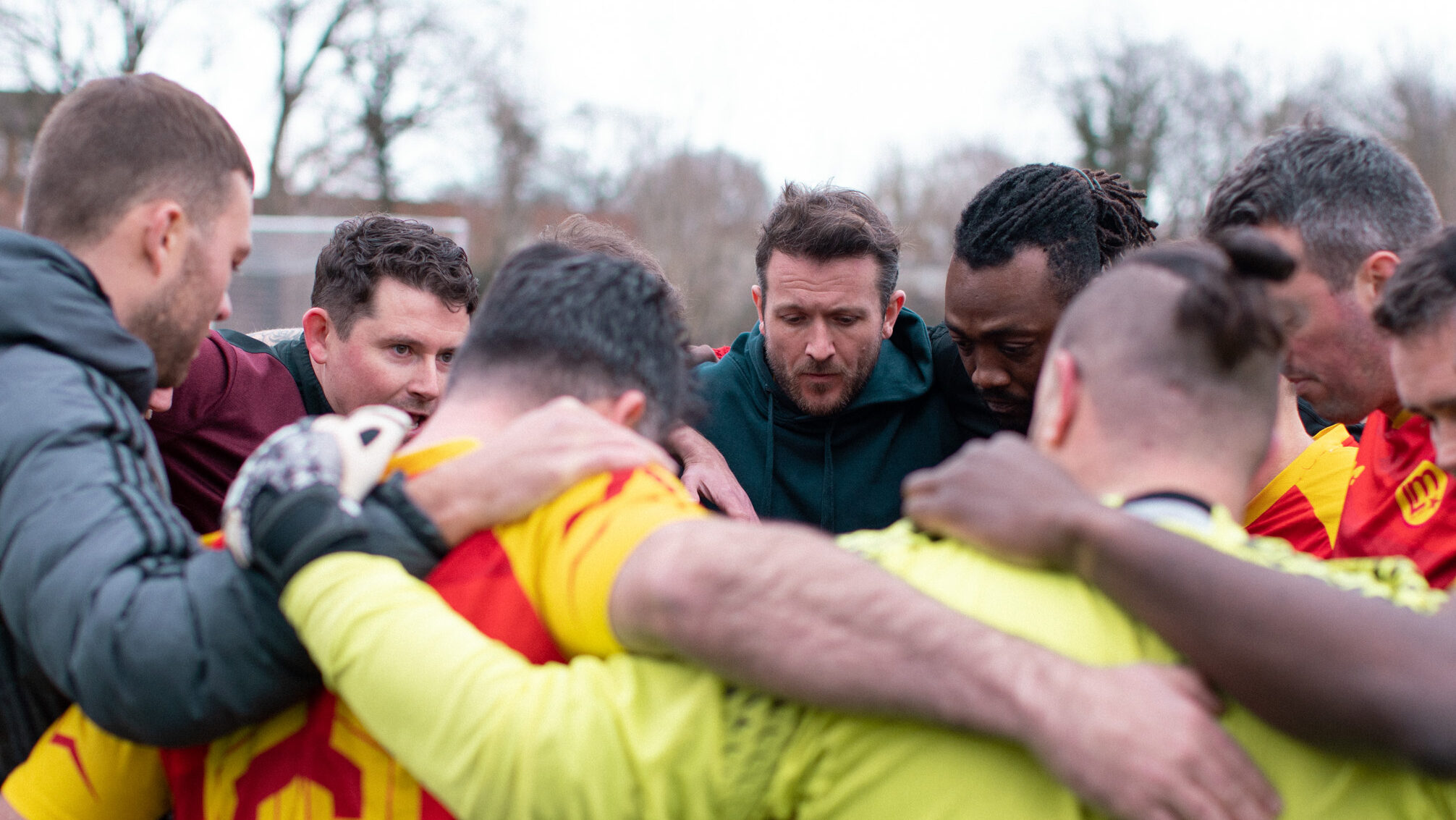 A group of men huddle in a circle wearing football jerseys