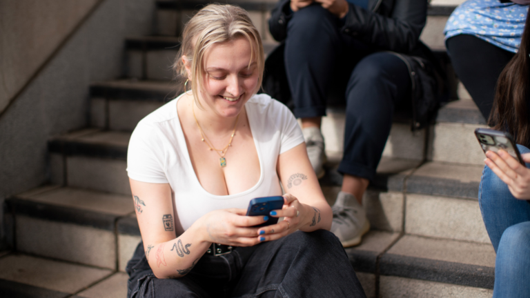 A woman sits on stairs holding her phone. There are 3 other people also on the stairs with their faces out of frame.