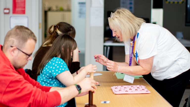 A teacher shows three students across a desk how to use a condom on a demonstrator