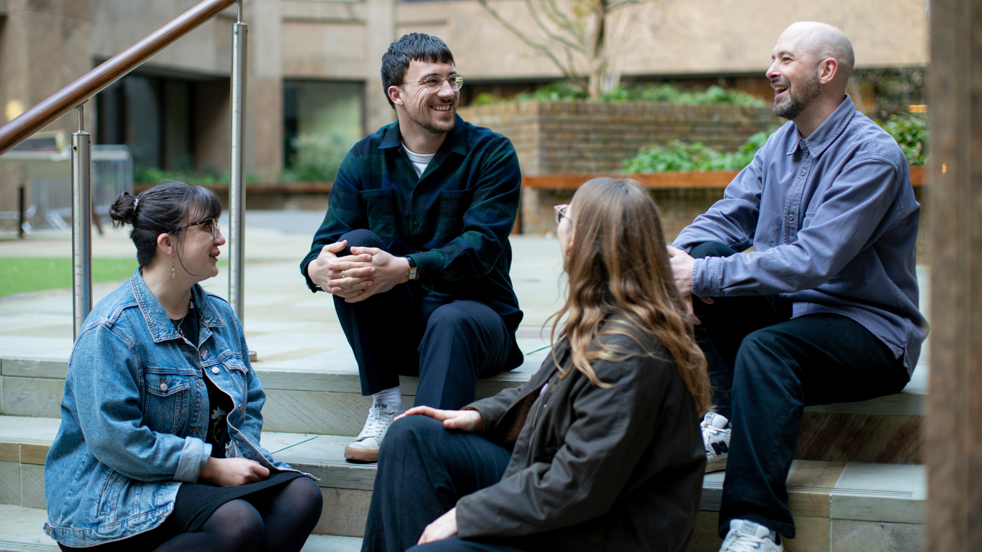 4 people sit on stairs outside, smiling and chatting