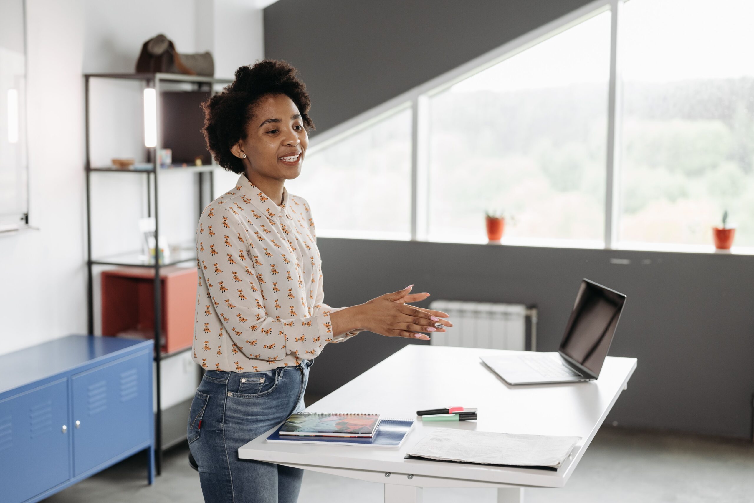 Woman stood at front of room talking with laptop in front  of her