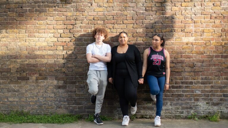 three young people lean against a brick wall